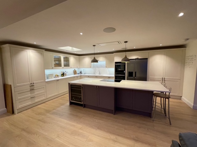 Modern kitchen interior with recessed ceiling lights and pendant lamps above a central island, showing professional electrical installation.